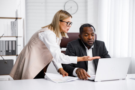 Angry female boss scolding African American office worker. A demanding manager-leader is annoyed by laziness and mistakes in the work of an employee. Authoritarian leadership, malfeasance, racismの写真素材