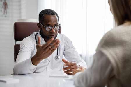African American doctor, receives a patient, listens to complaints, makes diagnostics. Writes data. Doctors appointment.の写真素材