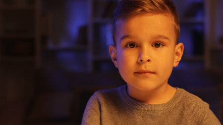 Portrait of a cute little boy sitting in his room in the evening looking at the camera. Close view.の写真素材