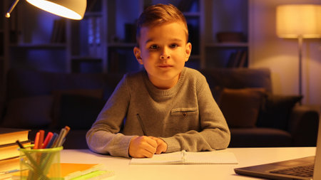 Portrait of a little boy student doing homework in the evening looking at the camera and smiling.の写真素材