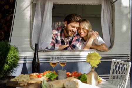 A lovely couple are standing in the sun, looking out the window of a tourist trailer, enjoying their vacation. People in love enjoying a sunny day outside the city, drinking wine.の写真素材
