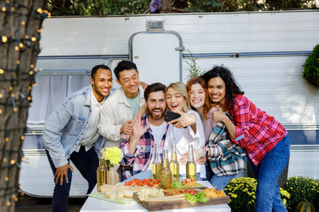 Mixed race friends taking selfie on mobile phone, outdoor party on travel trailer background. Rest outside the city. Happy people enjoy. Weekends in the summer time.の写真素材
