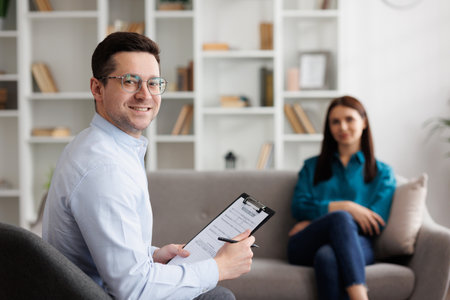 Portrait of professional psychologist consults a female patient in a state of stress and depression, who is sitting on sofa in the office. He writes on paper. The concept of a consultant psychologist.の写真素材
