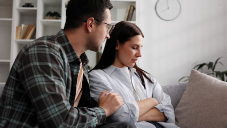A sympathetic young man provides psychological support to a thoughtful upset loved woman in a difficult life situation, showing loving care, overcoming grief together, or apologizing indoors.の写真素材