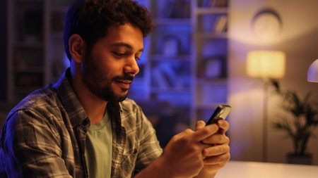 Smiling pretty young Arabian brunette boy holding mobile phone and credit card sitting at the table. Happy man makes online shopping using mobile payment. E-banking app service.の写真素材
