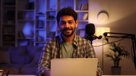 Portrait of young confident Arab man playing online computer video game, live streaming at home, smiling and looking at camera. Gamer lifestyle, E-Sport online gaming technology concept.の写真素材