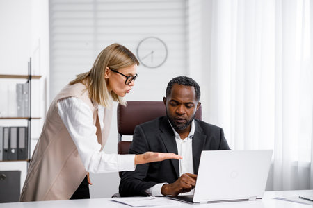 Angry female boss scolding African American office worker. A demanding manager-leader is annoyed by laziness and mistakes in the work of an employee. Authoritarian leadership, malfeasance, racismの写真素材