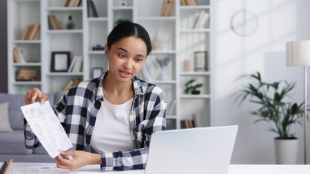 Attractive young woman works from home, has a video call with colleagues, shows graphs. Attractive young African American female student studying at home, giving a work presentation.の写真素材