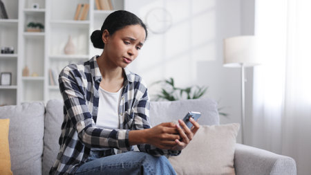 Worried young African American girl sitting on the sofa lookingの写真素材
