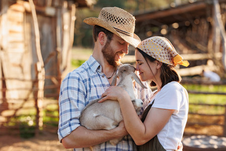 Portrait of young Caucasian happy farmer couple holding a little goat in their arms. Family business at ecological farm. Healthy food.Industrial production of goat milk dairy products. Cattle farming.の写真素材