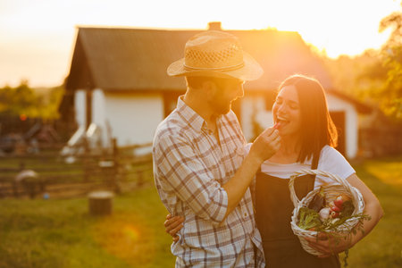 Portrait of young happy farmer couple holding basket with fresh organic vegetables on their rancho at the sunset. Vegetarian healthy food. Family business. Ecological farm and agriculture business.の写真素材