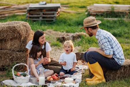 Happy young family having lunch at summer garden party. Mother, father and two kids enjoy spending time together on weekend at the countryside. Picnic with organic home-grown food. Healthy lifestyle.の写真素材