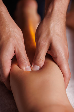 Male masseurs hands press female visitors leg, relaxing massage in spa salon. Body care for young woman.Therapeutic procedure for an injured leg, restoration of health.の写真素材
