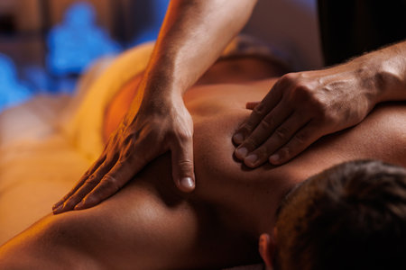 Physiotherapist massaging male patient with damaged shoulder muscle, treating sports injuries. Relaxing professional shoulder massage in cozy atmosphere, reboot on the weekend, end of difficult week.の写真素材