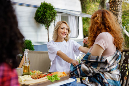 Two friends are having fun at a picnic table. A blonde and a redhaired girl are hugging on a picnic in the forest outside the city.の写真素材