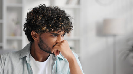 Sad upset Indian man sitting in his living room, thinking about the burdens of life and problems at...