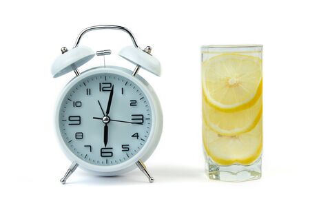 Alarm clock and a detox glass of water with lemon on a glass table. Wake up early in the morning by the alarm bell. Intermittent fastind diet concept.の写真素材