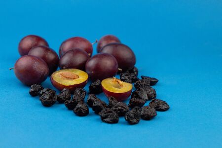 Fresh ripe plums, whole and halves, and dried prunes on a blue background.の写真素材