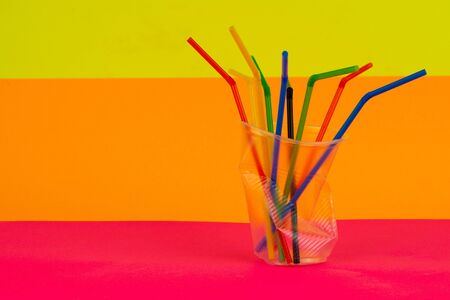 Empty crumpled plastic disposable cup with colorful straws on a multi-colored background. Concept of garbage and Environmental pollution.の写真素材