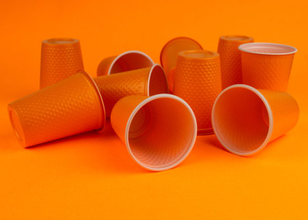 Set of orange plastic disposable cups on an orange background. Waste concept. Minimal space.