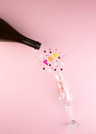 Festive Champagne bottle with colorful glittering stars splashes on pink background. Flat lay. Minimal party concept.の写真素材