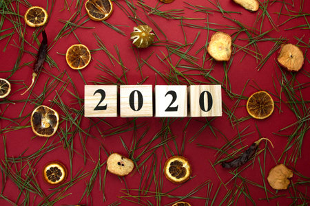 Wooden cubes with the inscription 2020 on a red background with pine needles and dry oranges.