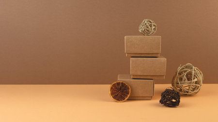 Christmas geometric banner. Craft gift boxes, balls from vine and slice of dry orange on pastel sand...