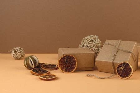 Christmas Craft gift boxes, balls from vine and slice of dry orange on pastel sand color background.. Eco concept. Recycled paper and natural eco materialsの写真素材