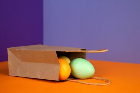 Easter composition of multicolored colorful easter eggs on craft paper bag on pastel background. Happy Easter holidays. Flat lay.の写真素材