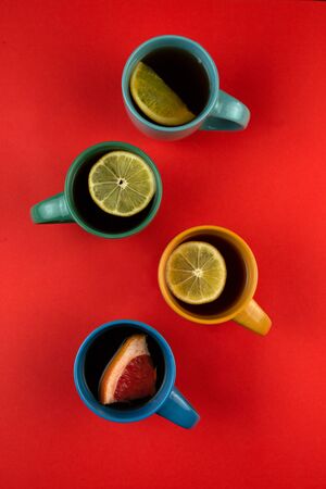 Many colorful mugs of tea and citrus fruits on a red background, top view. Lemon, pomelo, orange, citrus Sweetie, grapefruit.の写真素材
