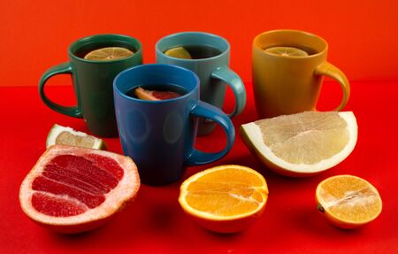 Many colorful mugs of tea and citrus fruits on a red background, top view. Lemon, pomelo, orange, citrus Sweetie, grapefruit.の写真素材