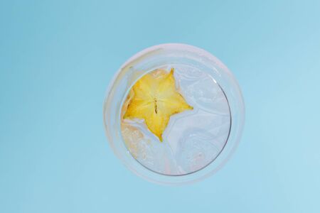 Glass of fresh iced cocktail decorated with starfruit slice on blue background. Vertical shot.の写真素材