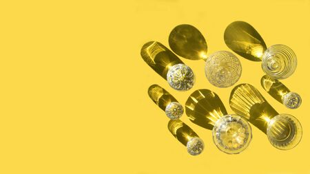 Glasses with clear water stand on a yellow background, top view. Beautiful creative still life is flooded with light with hard shadows and glare from the glass. Banner with place for text.の写真素材