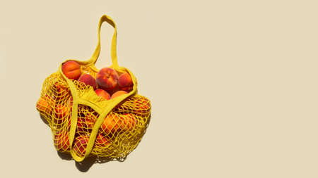 Ripe peaches in a mesh bag or string bag on light yellow background. Flat lay. Zero waste. Top view.の写真素材