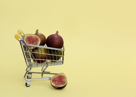 Shopping trolley with few figs on pastel yellow background. Vertical shot, copy space. Shopping of...