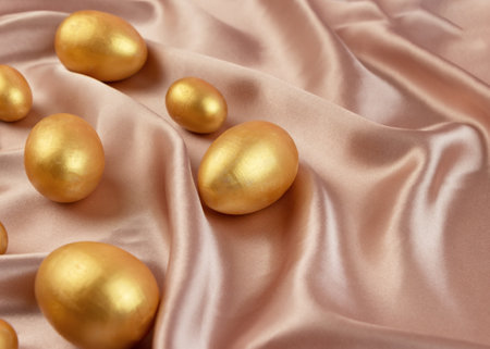 Golden decorative Easter eggs on a background of creamy shiny natural fabric. Soft texture concept. Champagne silk fabric. Happy Easter greeting card.の写真素材