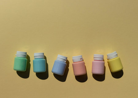 Cans of multi-colored acrylic paints in pastel colors in a row on a yellow background. A...