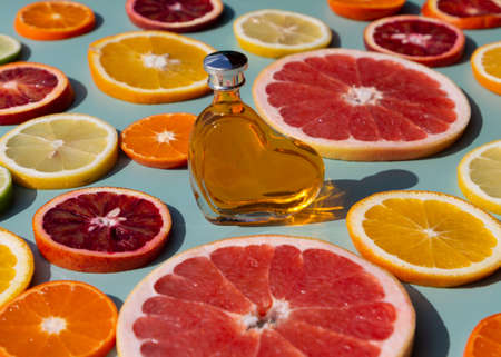 Vitamin C serum in a heart shaped bottle on a slised citrus set. Orange, grapefruit, lime, tangerine, lemon. Organic SPA cosmetics with orange oil. Hard shadow.の写真素材