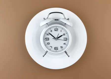 White alarm clock on an empty plate on beige background. Intermittent fasting concept.の写真素材