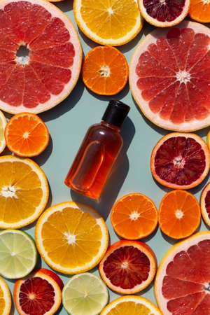 Vitamin C serum in a glass bottle on a slised citrus set. Orange, grapefruit, lime, tangerine, lemon. Organic SPA cosmetics with orange oil. Hard shadow.の写真素材