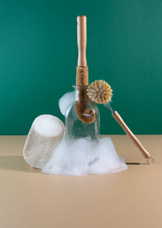 Reusable wooden dish washing brush with coconut bristle on a beige background with soapy foam. Place...