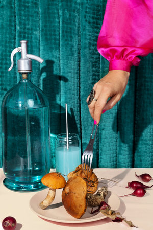 Food fashion aesthetics. A womans hand in a pink satin sleeve pricks forest mushrooms with a fork.の写真素材