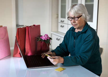 An attractive gray-haired 85 year old woman is shopping online. She is holding a credit card in her hand. Sales concept.の写真素材