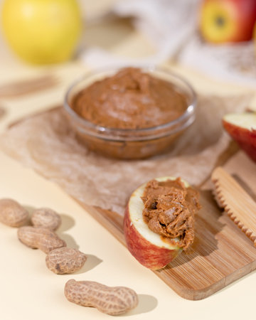 Peanut butter in a glass cup and ripe apples in a string bag. Spread the peanut butter on the apple...
