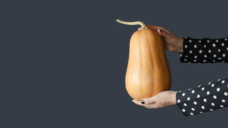 A woman in a black dress with white polka dots holds a beautiful orange pumpkin in her hands. Minimalism, fashionable Halloween.の写真素材