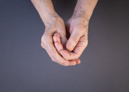 Hands of an elderly woman rubbing her sore fingers on a gray and purple background.. Arthritis...