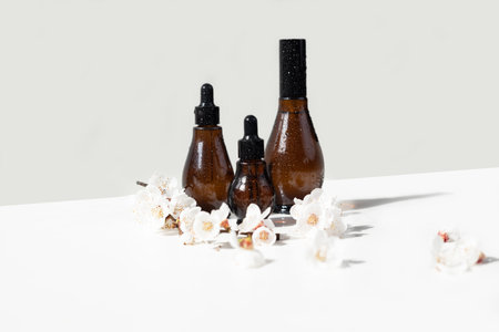Convex amber glass dropper bottles with black lid and cherry flowering branch on white. natural...