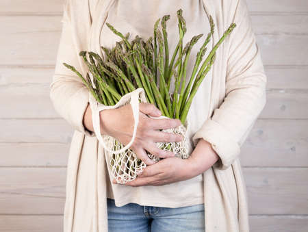 A woman holds a large bunch of fresh green asparagus in her hands. Healthy food and diet. Support for local businesses.の写真素材