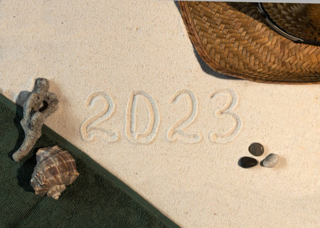 Numbers 2023 handwritten in the sand surface. New year concept photo. Straw hat and seashells frame