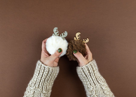 The hands of a woman in a woolen knitted sweater hold fluffy fur Christmas balls. Cozy winter fluffy new year concept. Natural earth colors brown and white, no plastic.の写真素材